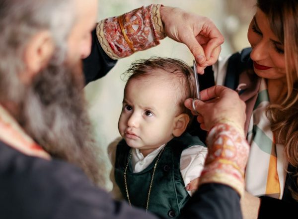 A baby's first haircut performed during a religious ritual with parents and clergy present.